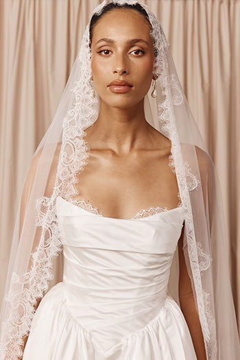 model wearing mantilla veil paired with basque waist satin wedding dress