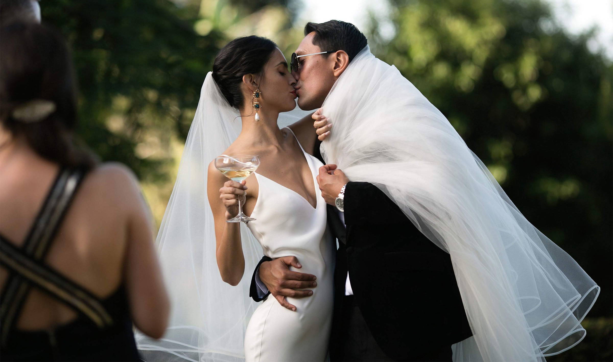 Bride wrapping her groom wearing sunglasses up in her tulle veil