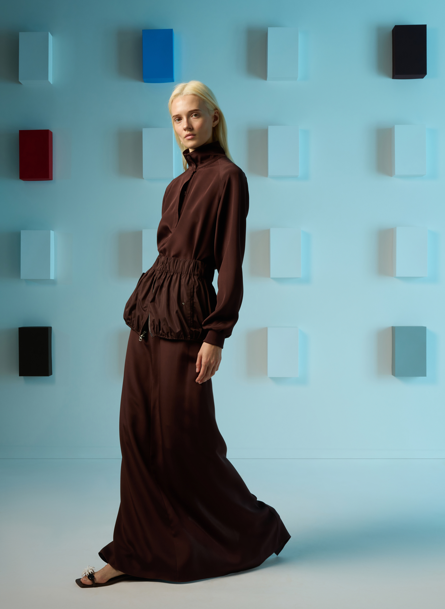 Model in a brown dress posing against a colorful background.