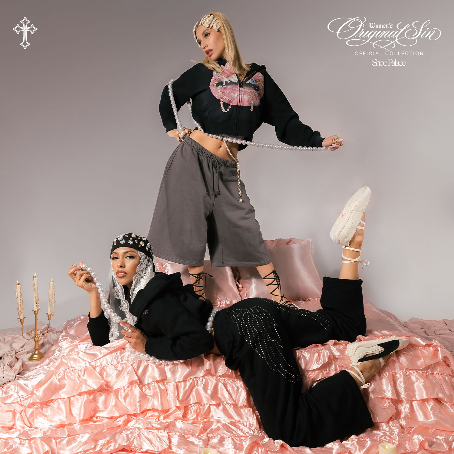 Two fashionable individuals posing on a pink fabric backdrop with candles.