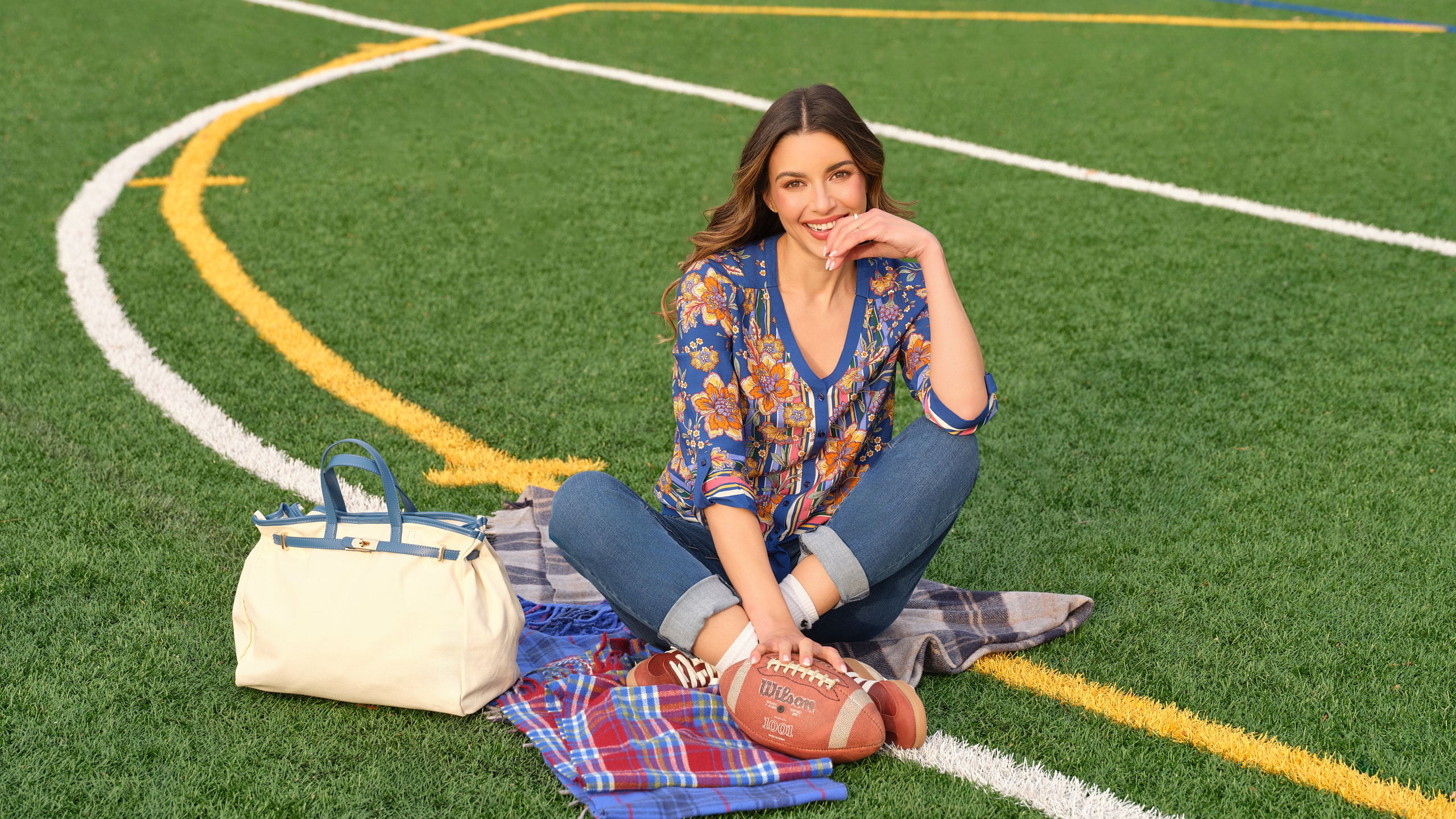 Woman sitting on a field with a football and a bag.