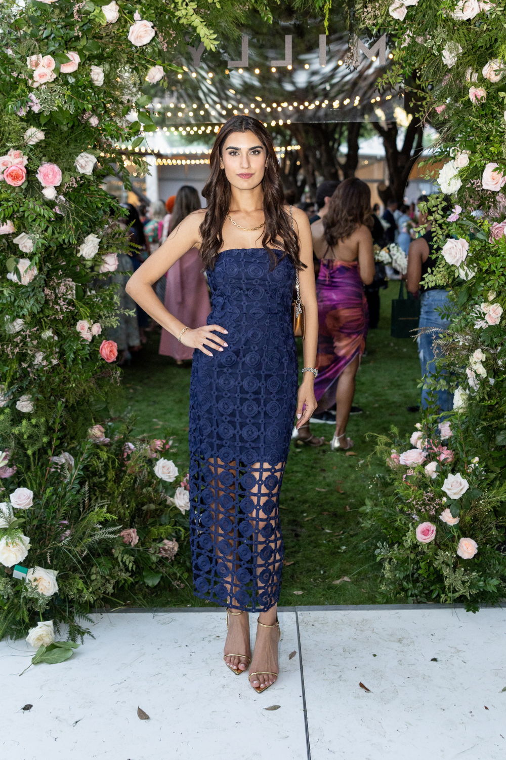 A woman in a navy dress stands in a floral archway.