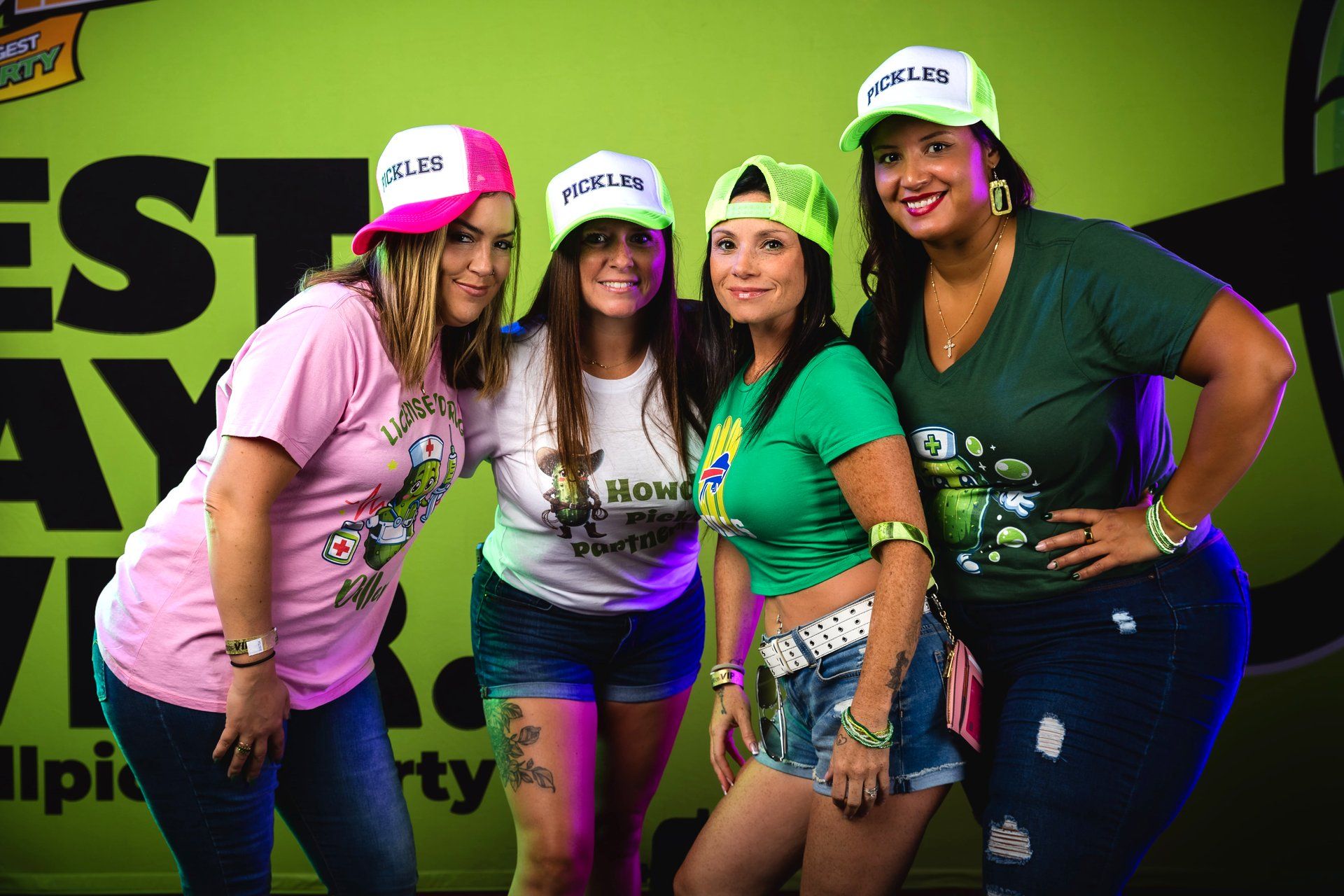 Four longtime guests in PICKLES trucker hats and pickle-themed merch return to the interactive photo booth as part of their annual tradition at The Big Dill pickle festival, Power Plant Live!, Baltimore Maryland 2025