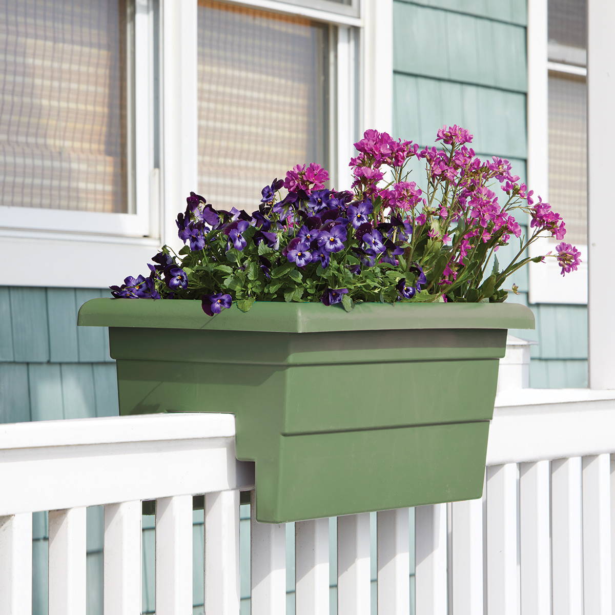 Flowers growing in a sage green railing planter on a white fence