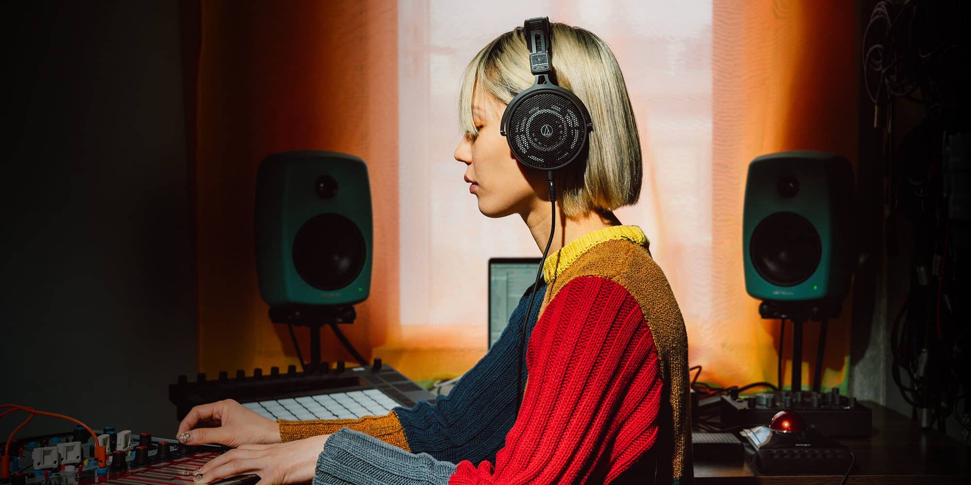 Woman wearing Audio Technica ATH-R50x headphones, working on music production in a studio.