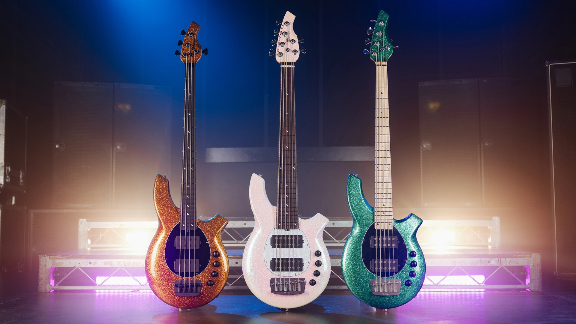 Three Music Man Bongo bass guitars in various colours on stage with colourful lighting.