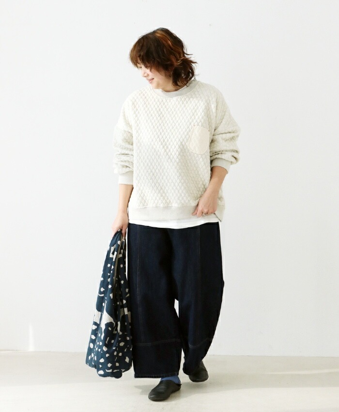 Person wearing a white sweater and dark pants, holding a patterned jacket.