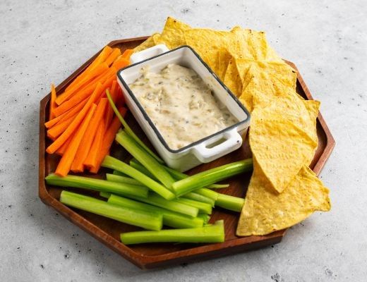 Vegetable sticks, tortilla chips, and dip on a wooden platter.