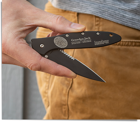 man holding a black Kershaw pocket knife personalized with a fingerprint, name, and dates