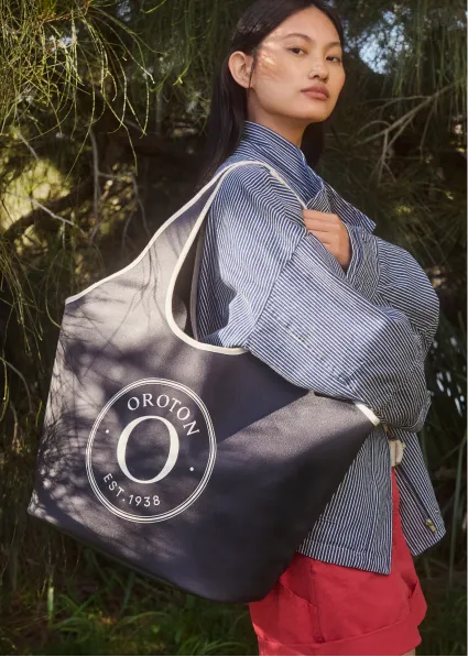 Model holding a large OROTON tote bag in a natural setting.