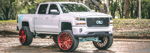 Front three-quarter Nick's lifted white Chevrolet Silverado with red wheels and teal suspension accents photo 1