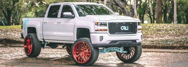 Front three-quarter Nick's lifted white Chevrolet Silverado with red wheels and teal suspension accents photo 1
