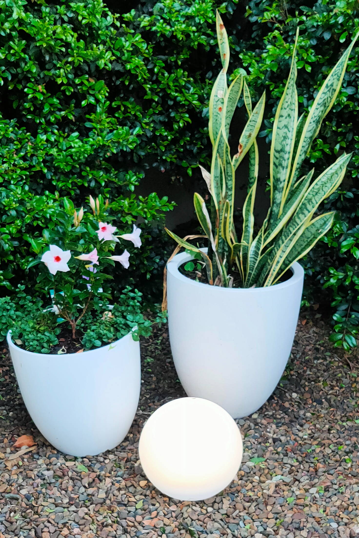 Two white pots with plants and a glowing orb on gravel.