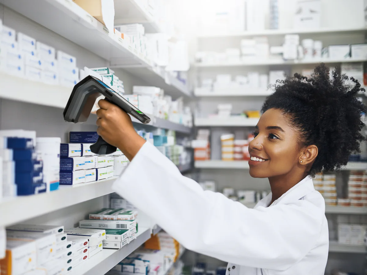 Personal de farmacia utilizando un lector frente a estantes con medicamentos