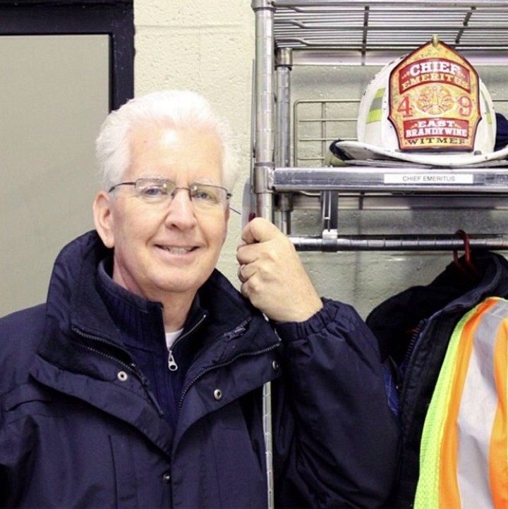 Smiling man in jacket beside a rack with fire safety gear.