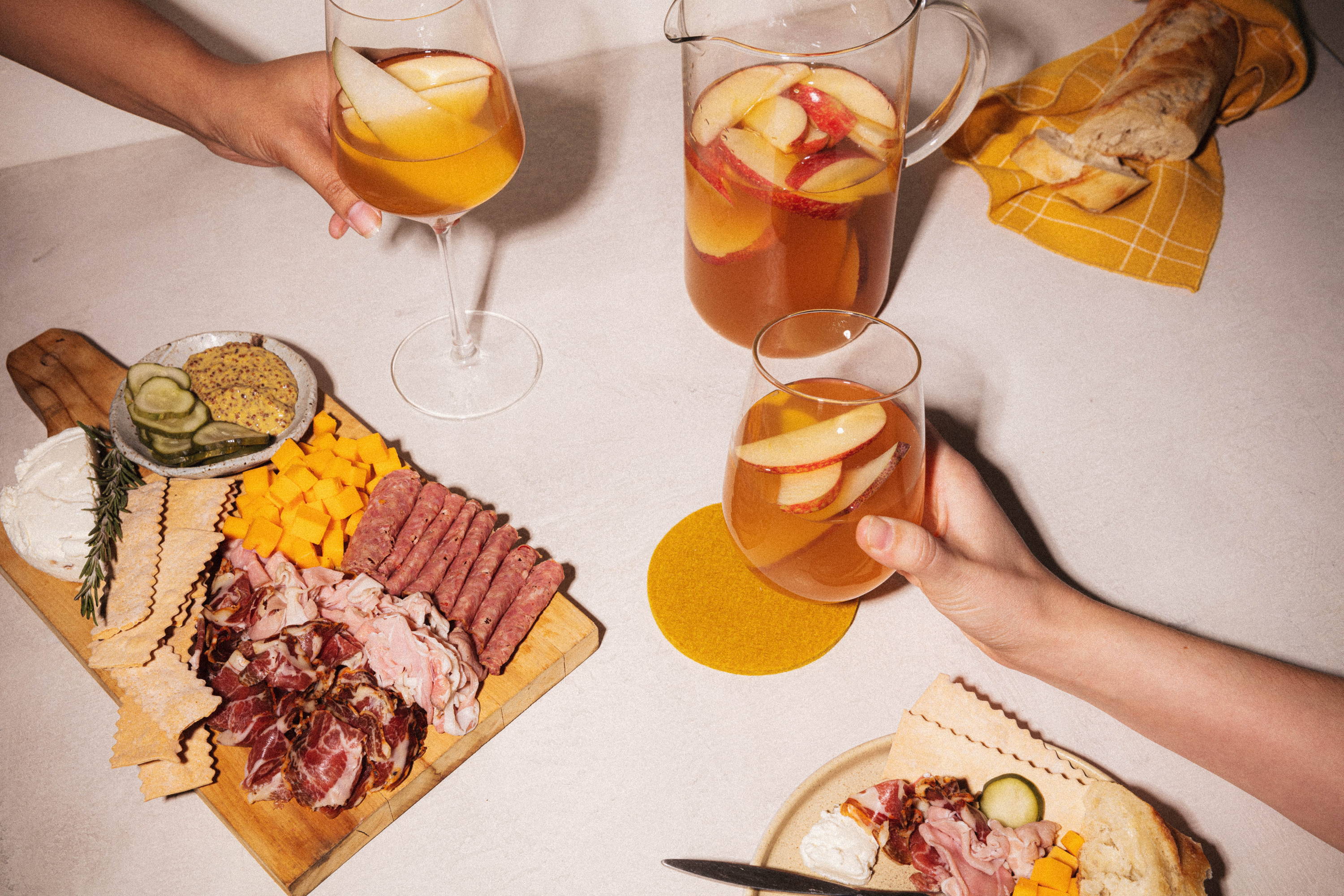 Holding wine glasses of apple cider with charcuterie board on table