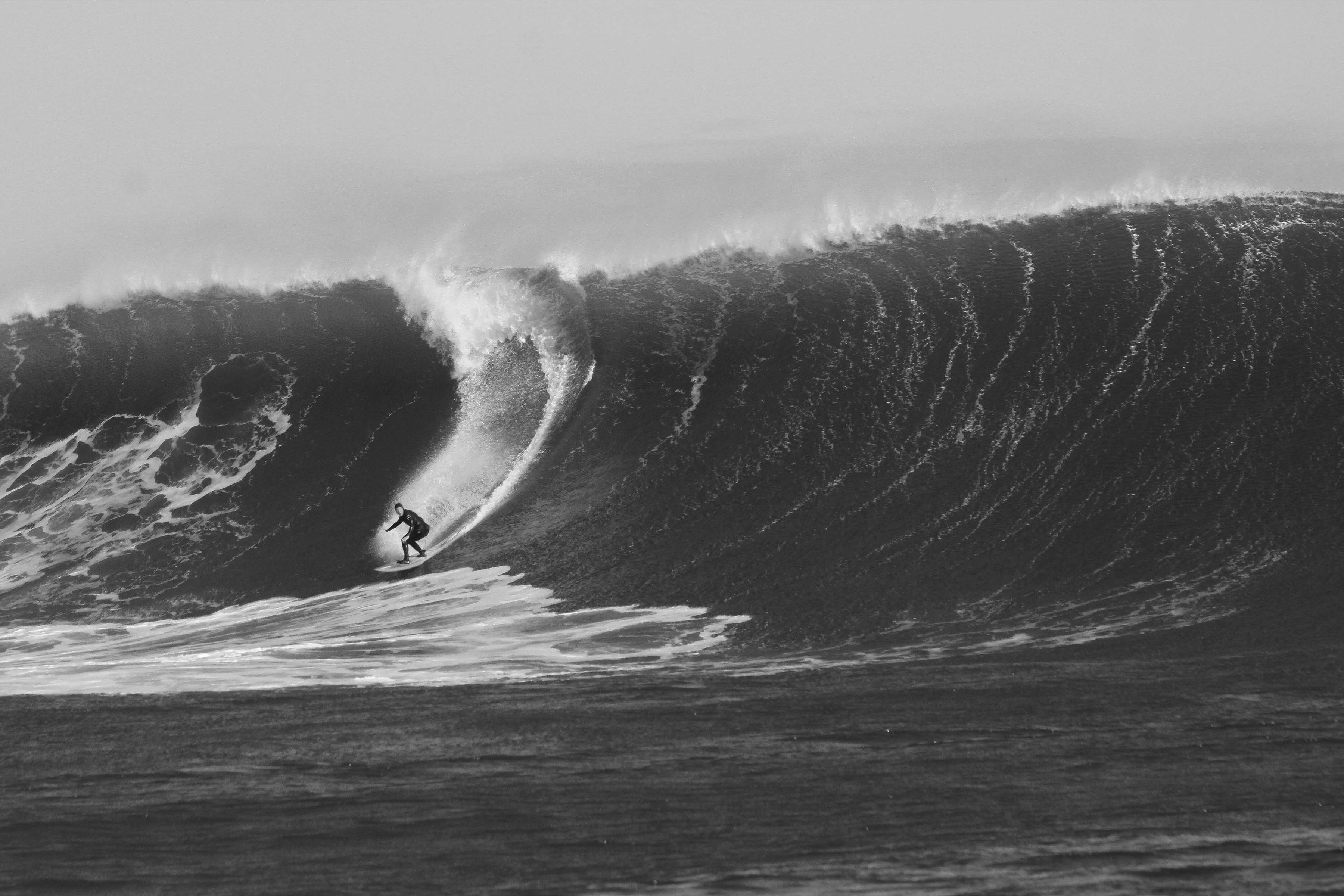 Surfer riding a large wave in black and white.