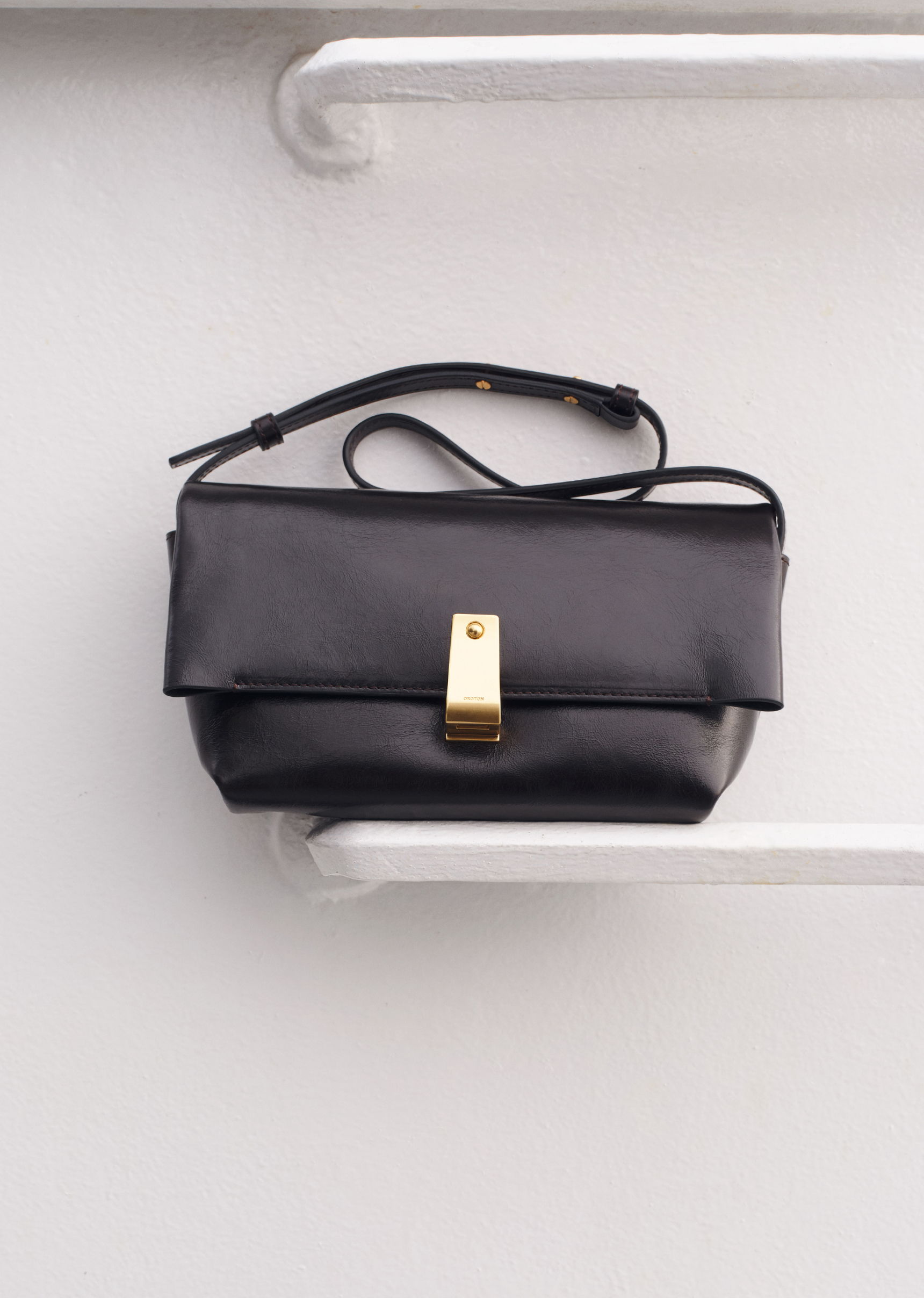 A black handbag with a gold clasp hanging on a shelf.