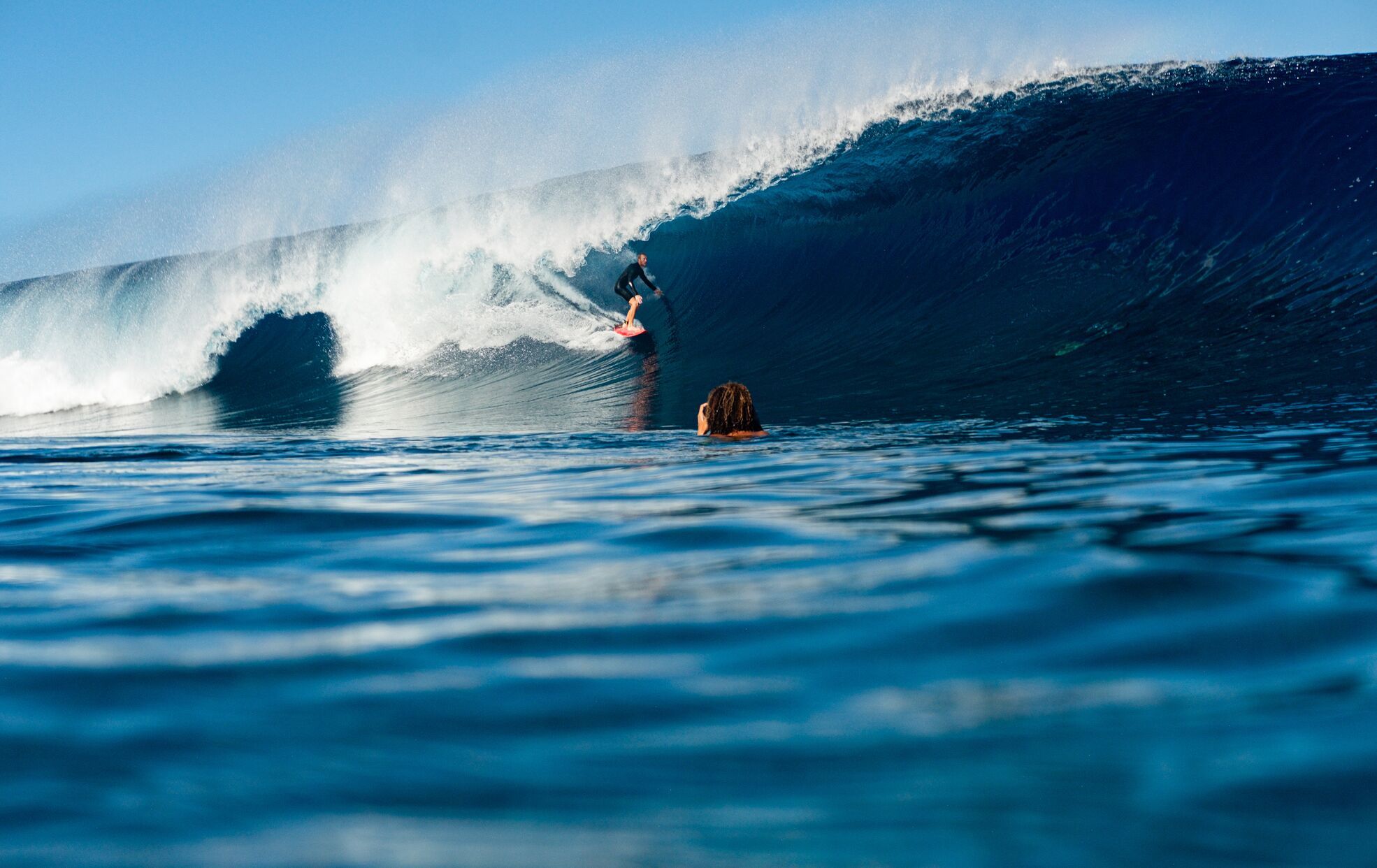 Surfer riding a wave with clear blue water in the foreground.