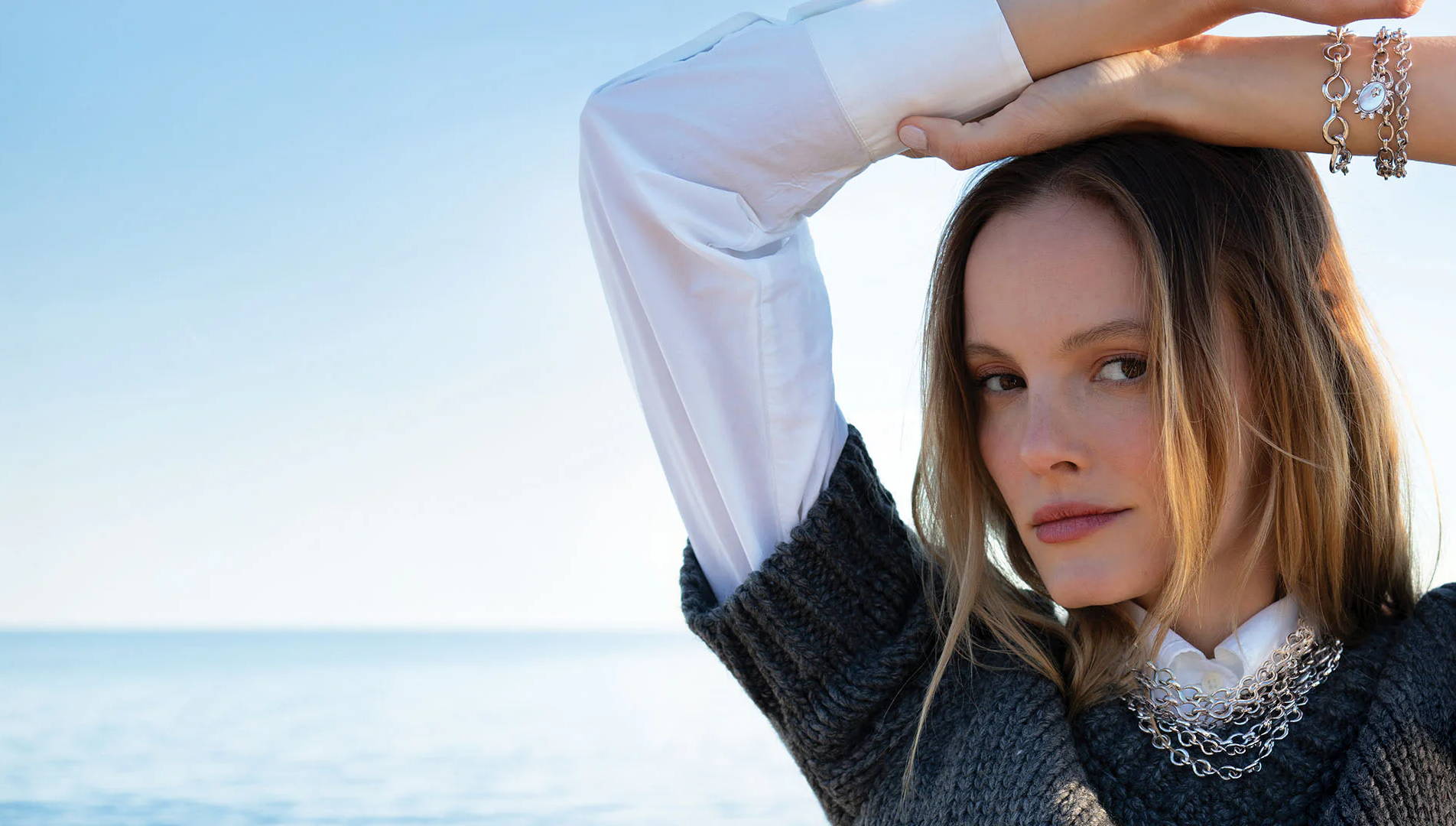 Woman posing with arms raised against a serene ocean backdrop.