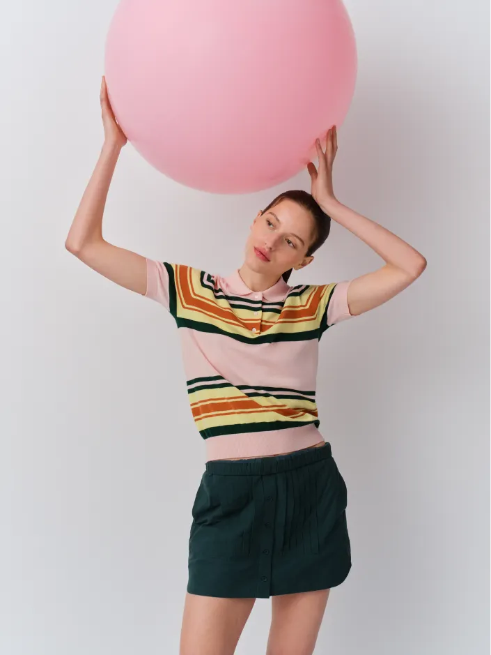 A woman holding a large pink balloon, wearing a colorful striped shirt and shorts.