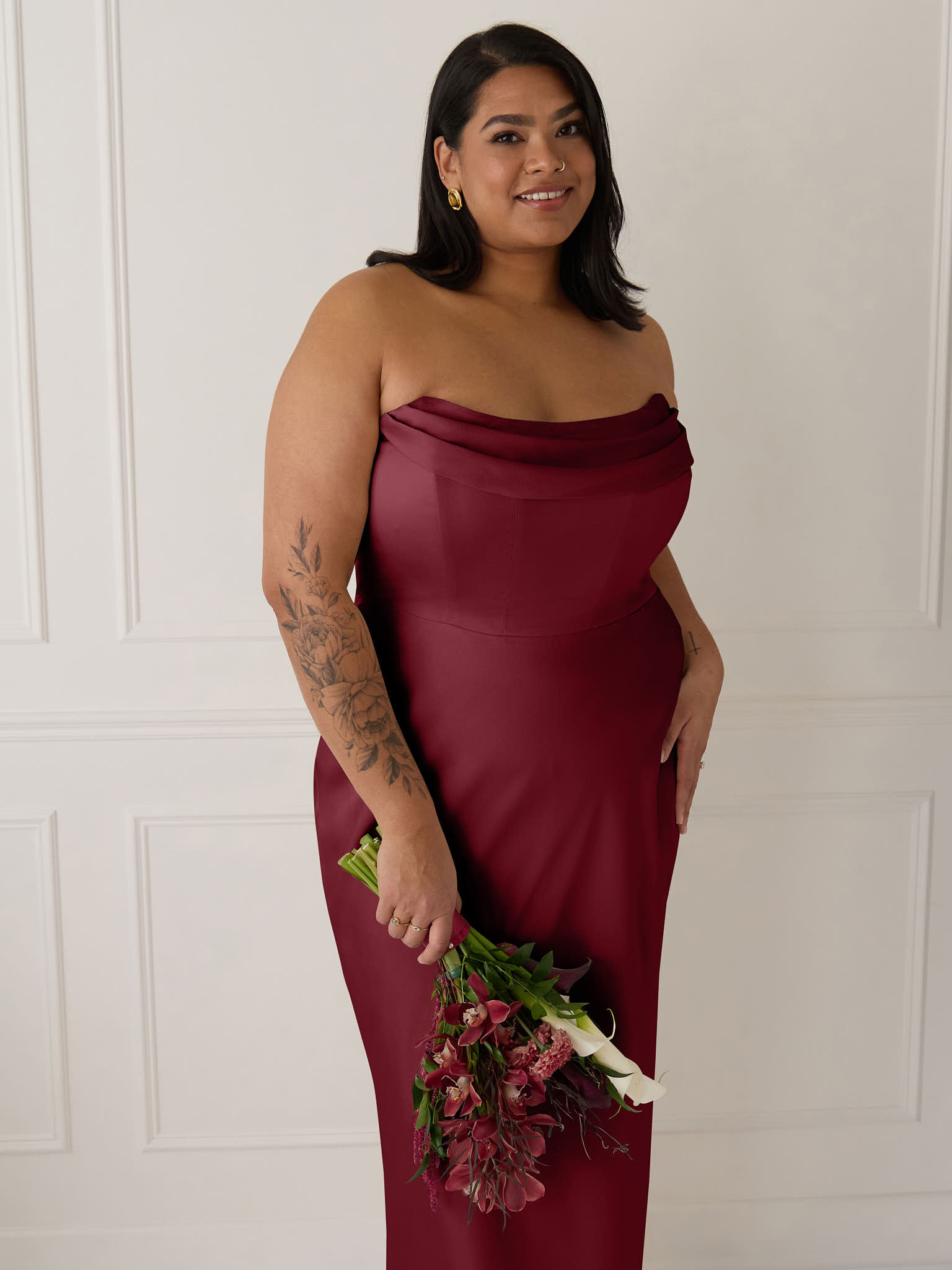 A woman in a burgundy strapless dress standing against a neutral background.