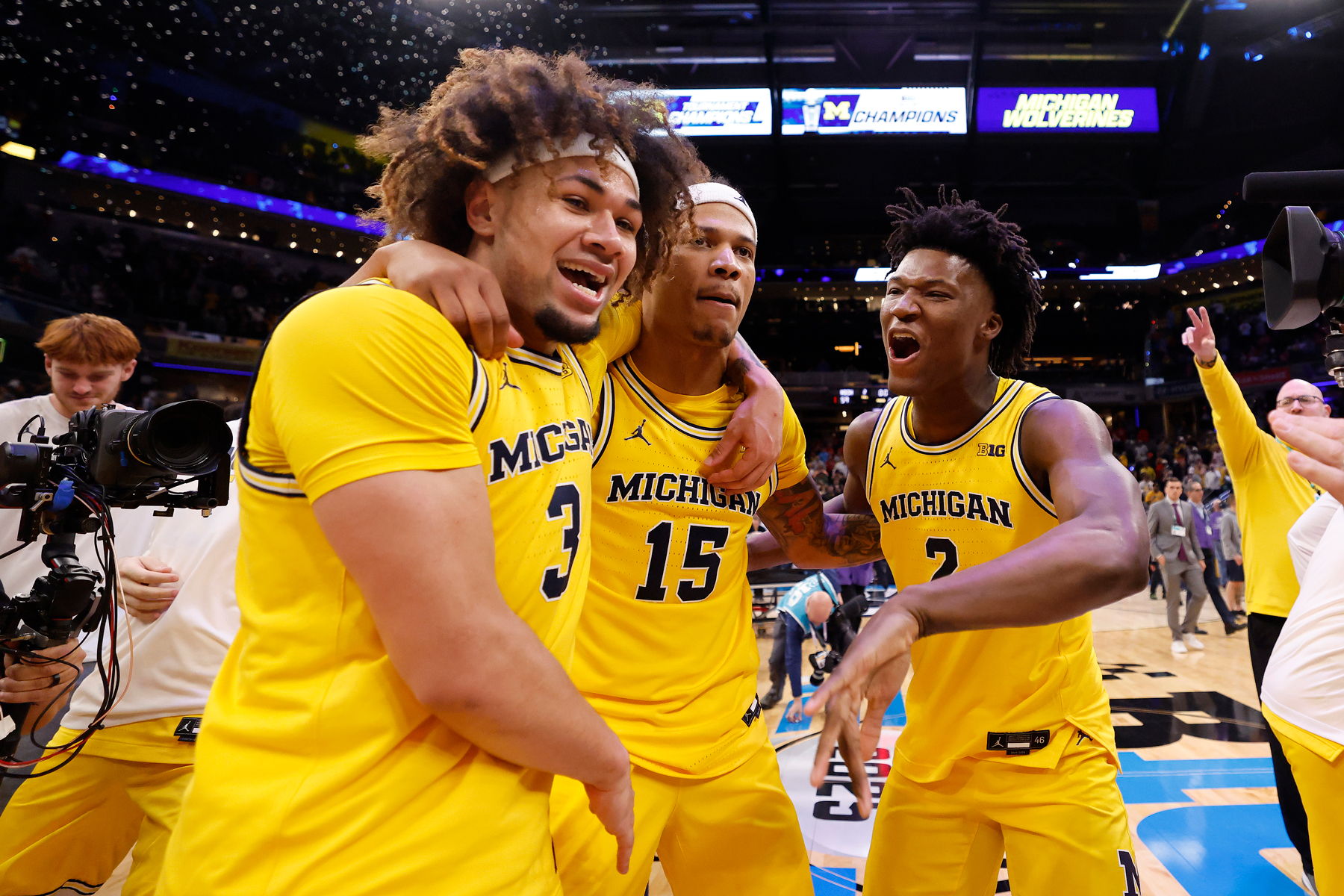Three basketball players celebrating in yellow jerseys after a victory.