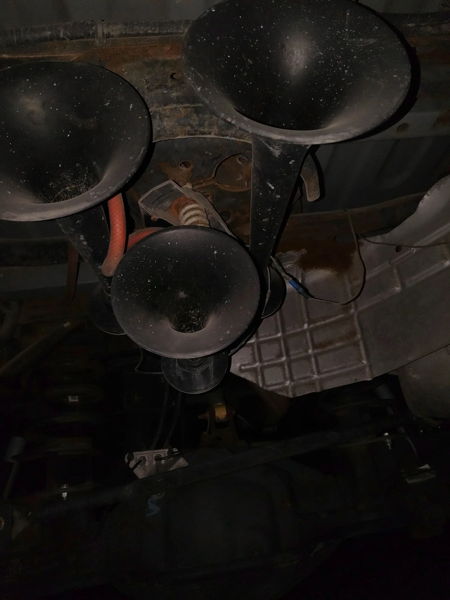 Undercarriage view of three black trumpet air horns mounted to vehicle frame with red air line