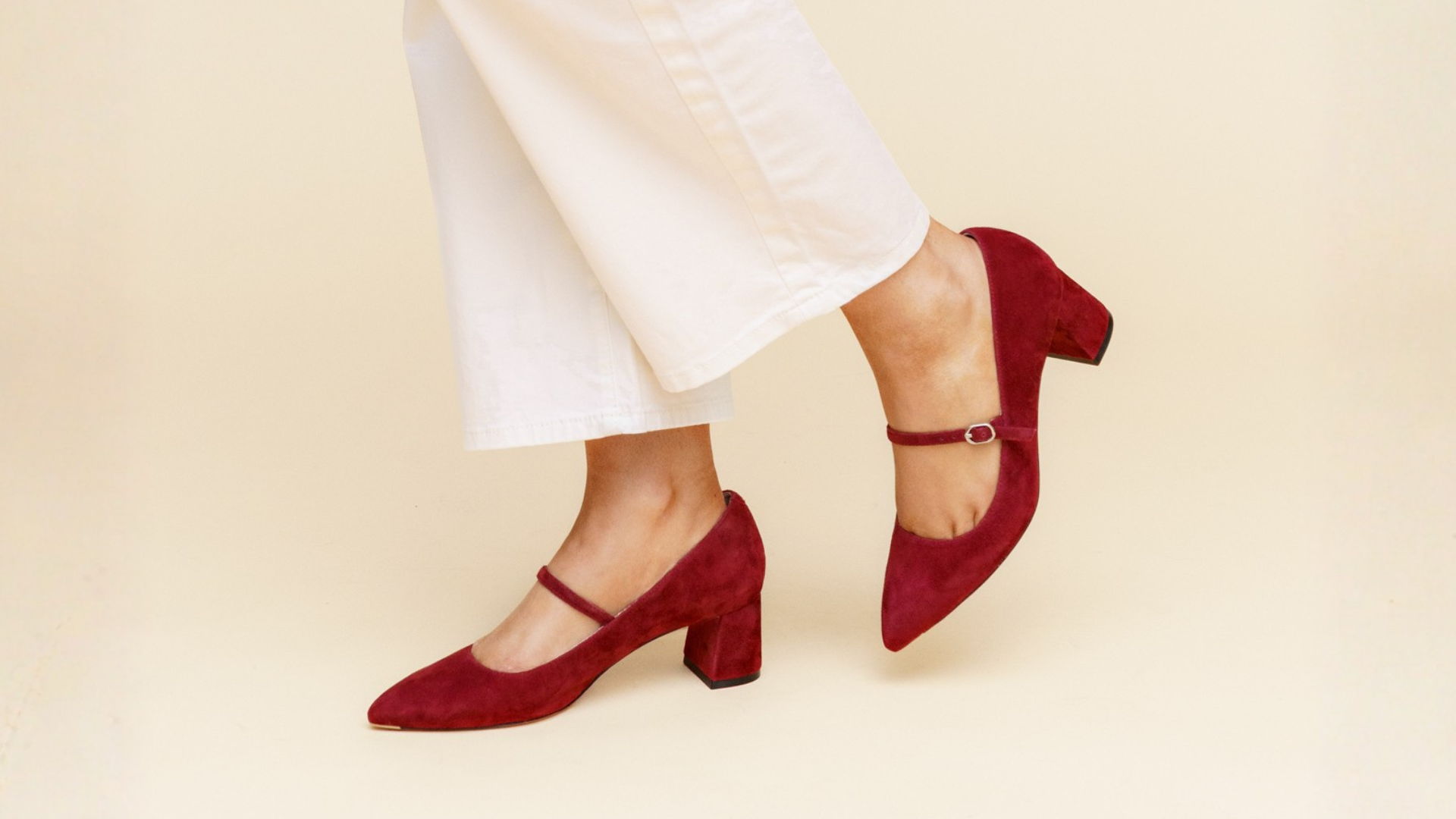 Red heeled shoes worn with white pants on a neutral background.