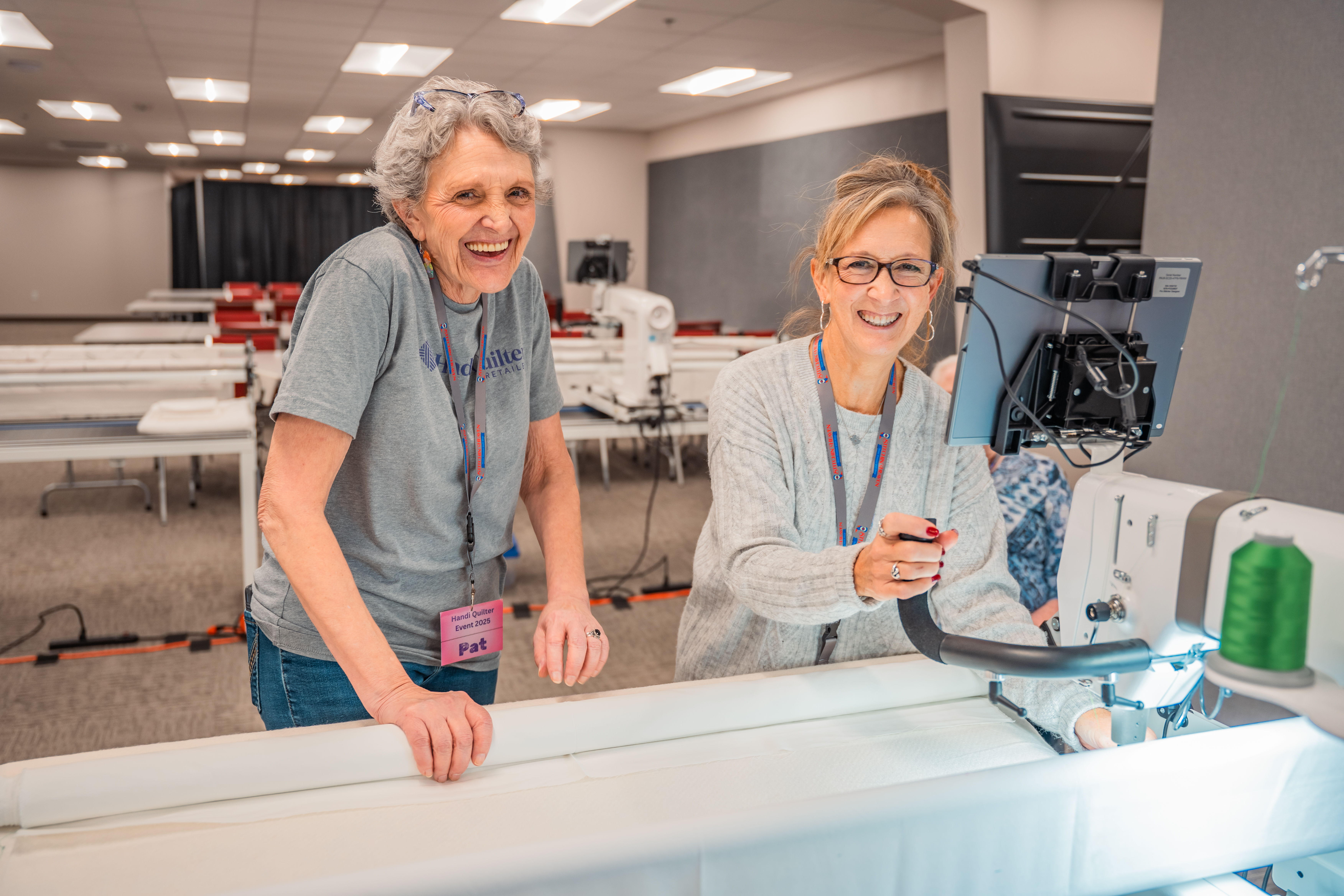 Two women smiling and working with a sewing machine in a bright room.