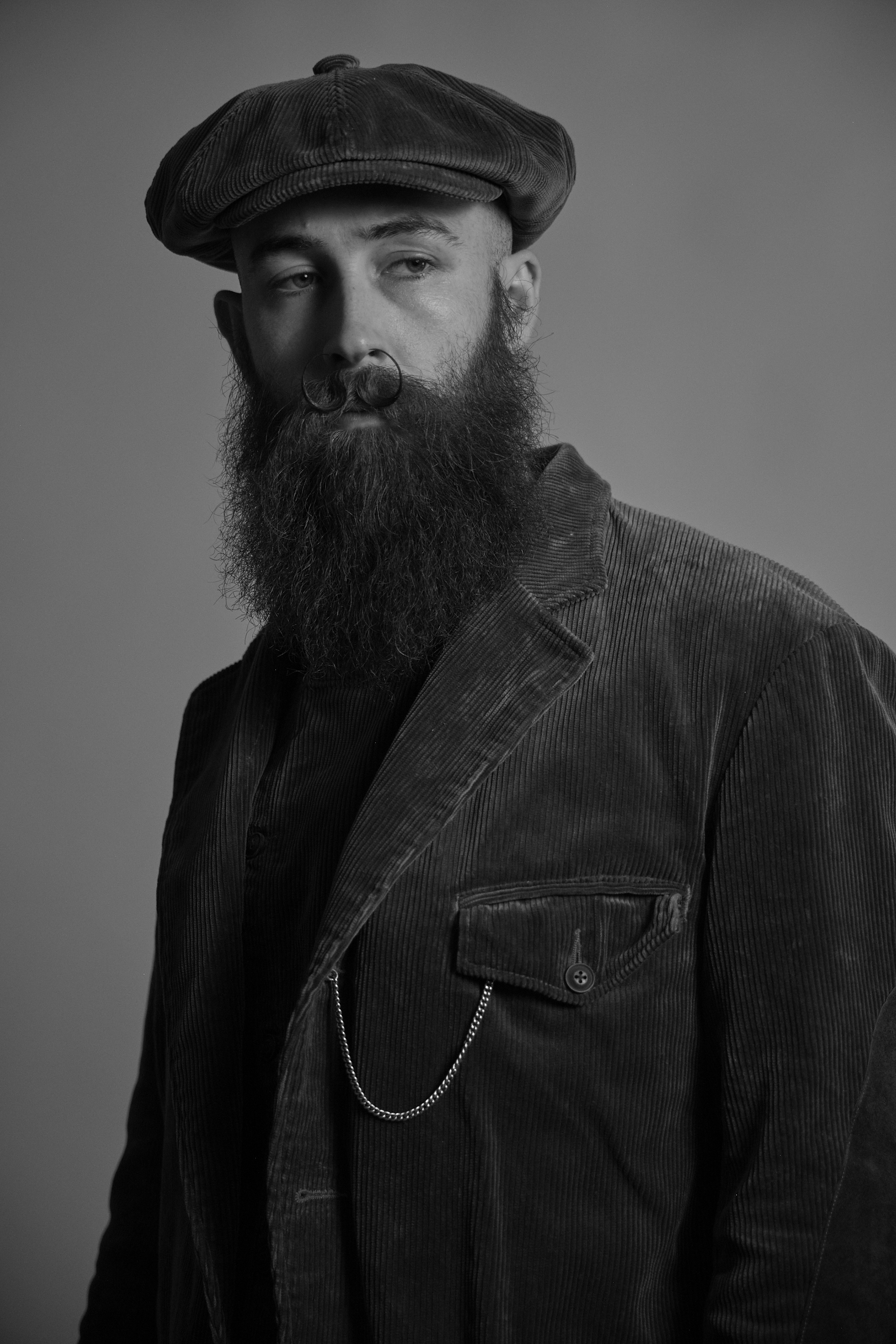 Man in vintage clothing standing near a wooden cart and logs.