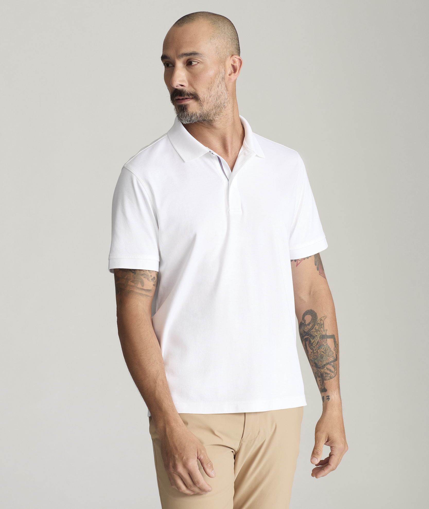 Man wearing a white polo shirt with short sleeves, standing against a neutral background.