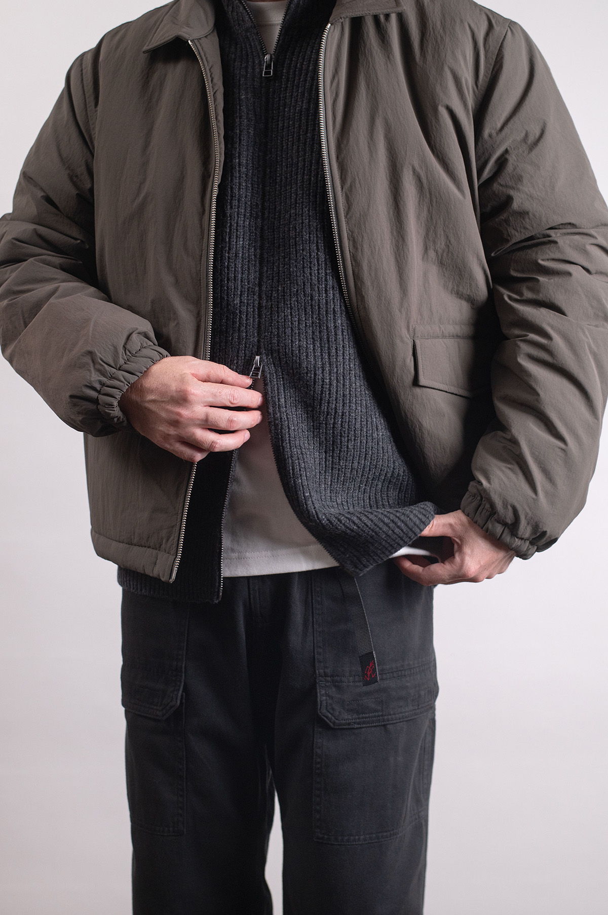 Person wearing a puffer jacket, sweater, black pants, and shoes on wooden floor.