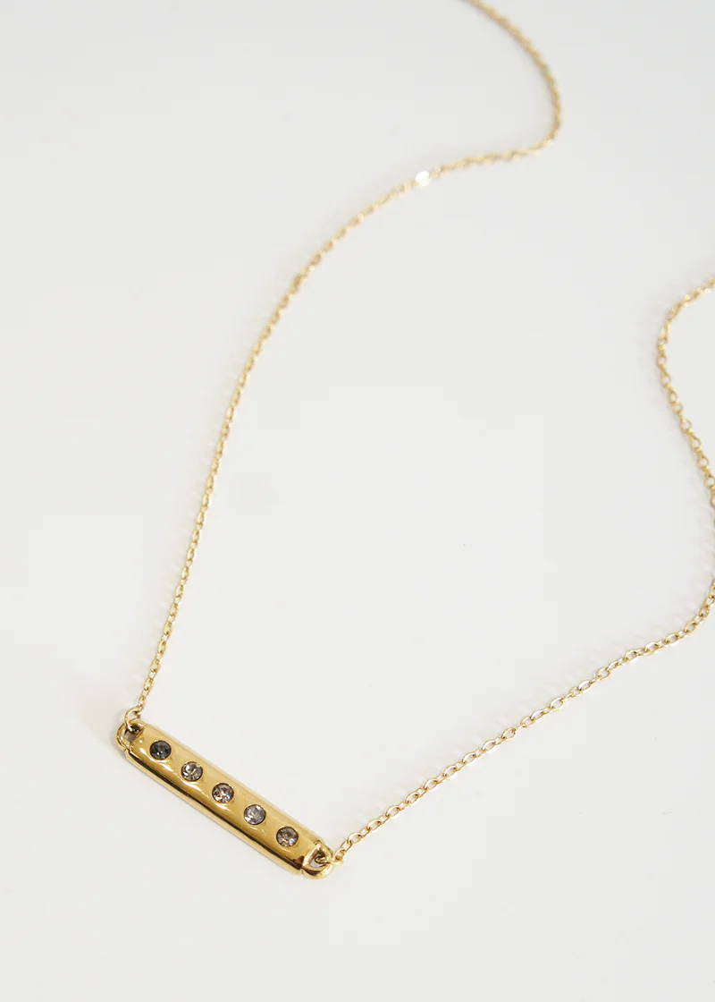 A simple gold necklace with a gold bar pendant with 5 clear crystal details