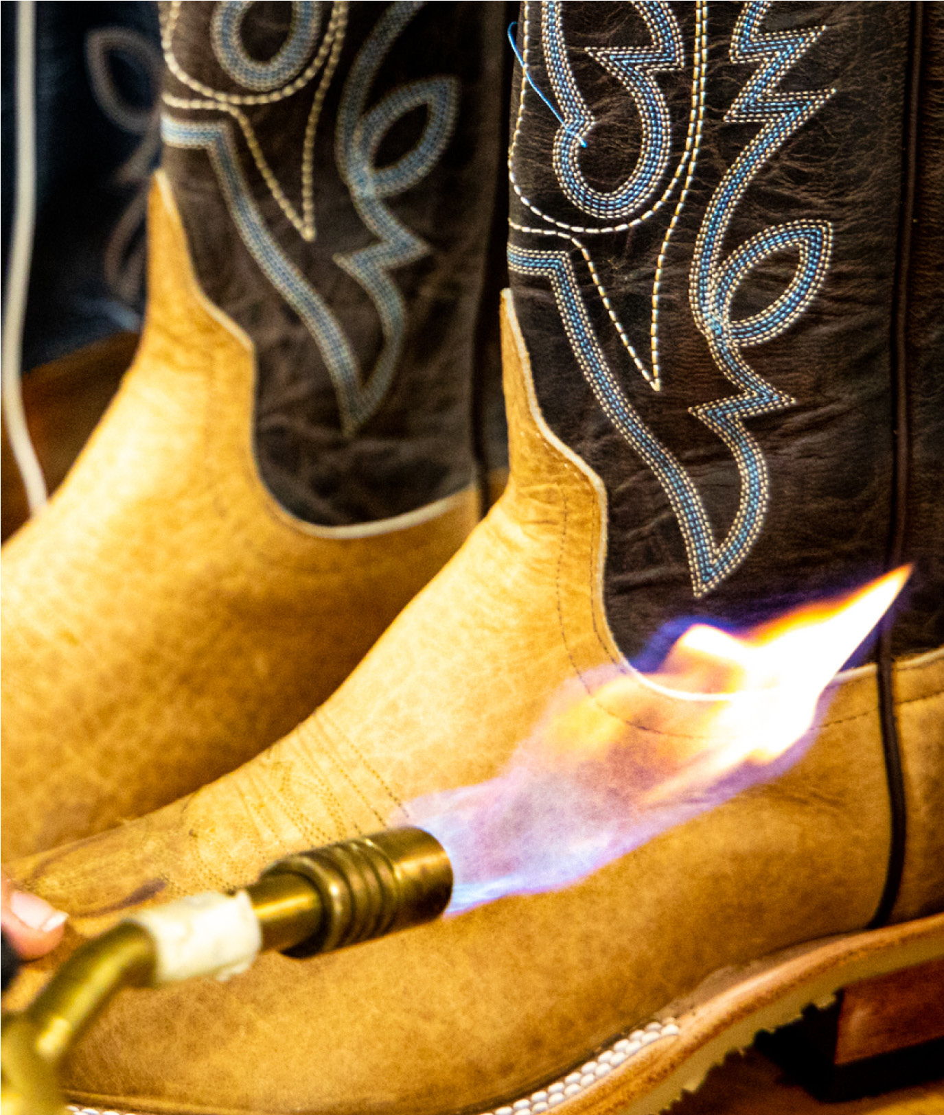 A hand using a flame to burnish cowboy boots.