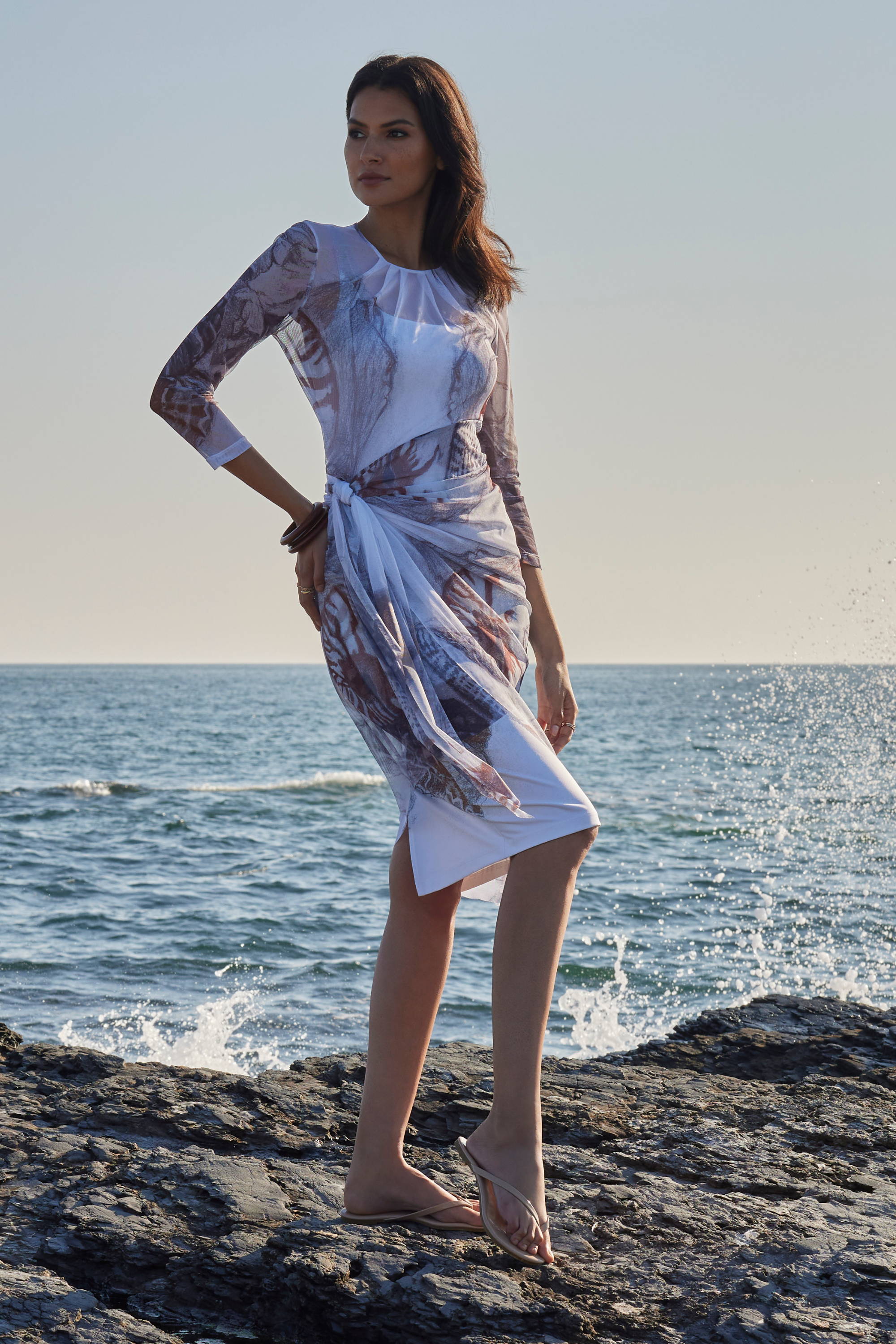 Woman wearing sarong mesh wrap dress over stretch knit dress by the ocean by Ala von Auersperg for resort 2024