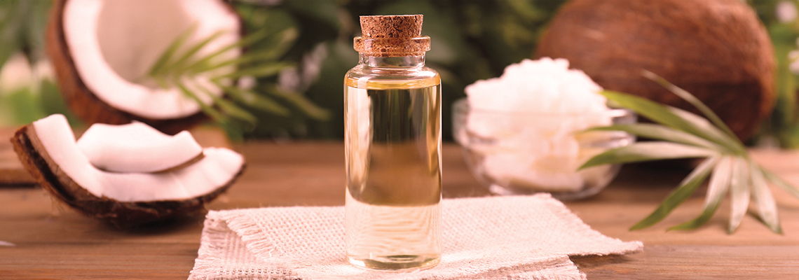 A bottle of oil surrounded by coconut and flowers on a wooden surface.
