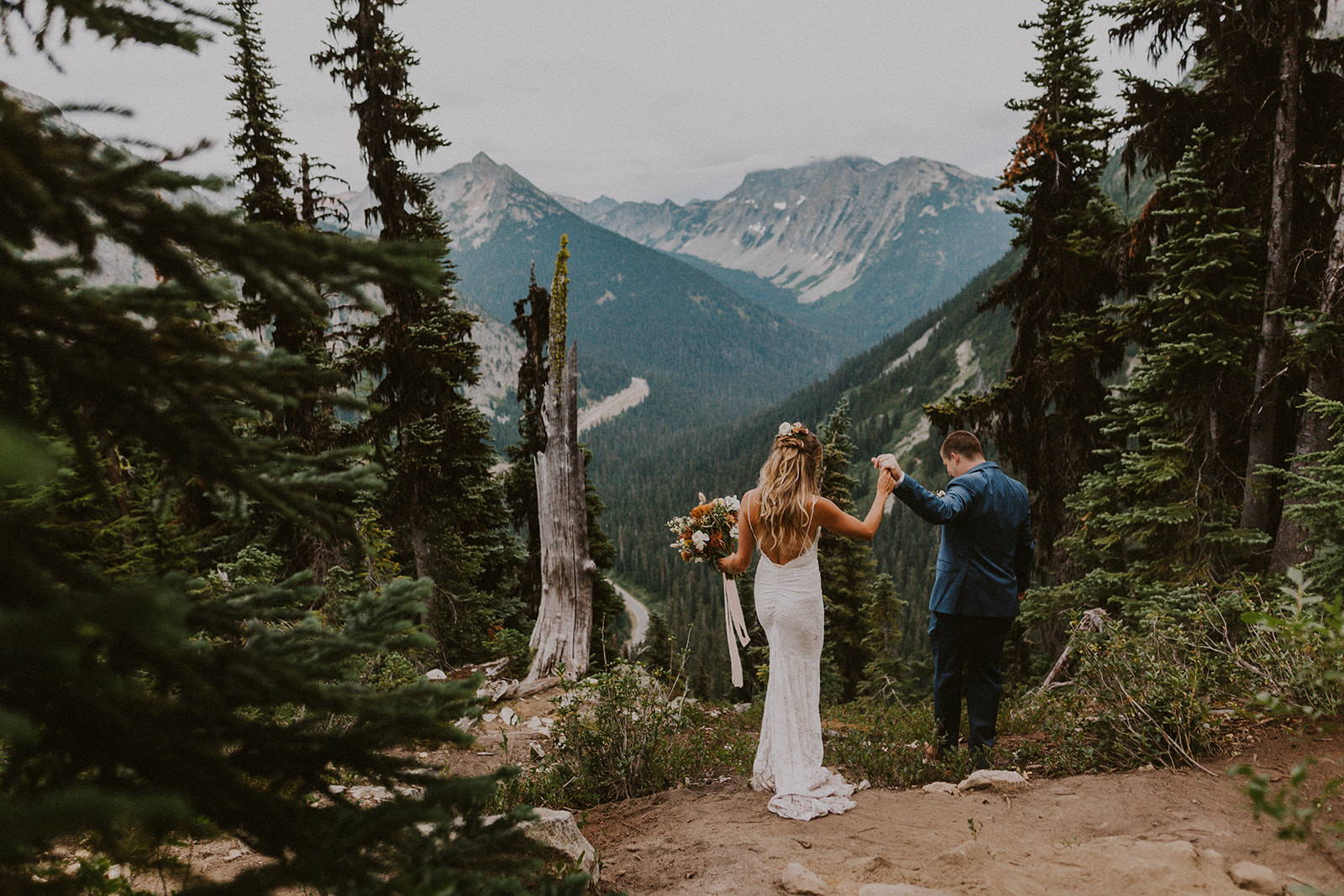 Bride wearing low back lace dress and groom in between trees in North Cascades National Park