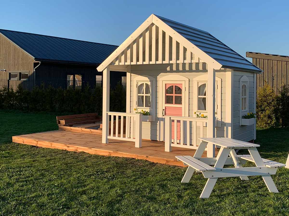 Custom Wooden Playhouse with metal roof, opening windows and white picnic table on green lawn by WholeWoodPlayhouses 