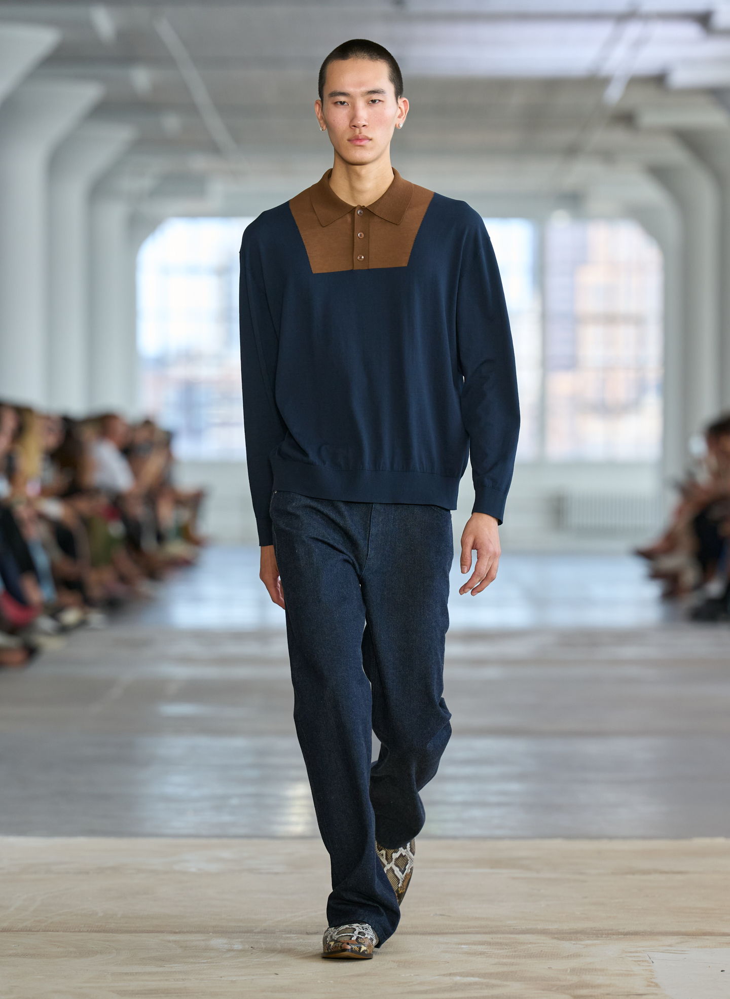 Model walking down runway in navy outfit with brown collar.