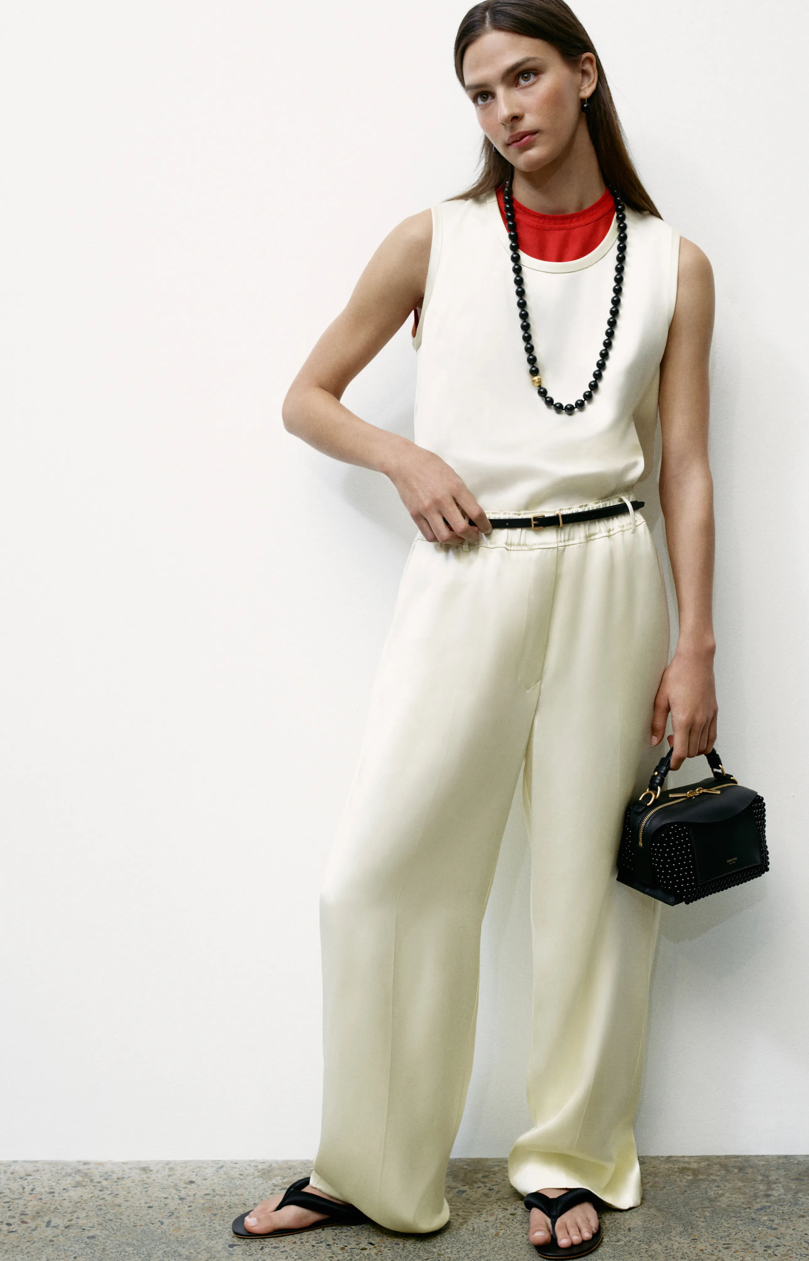 Model wearing a white outfit with red accents and a black handbag.