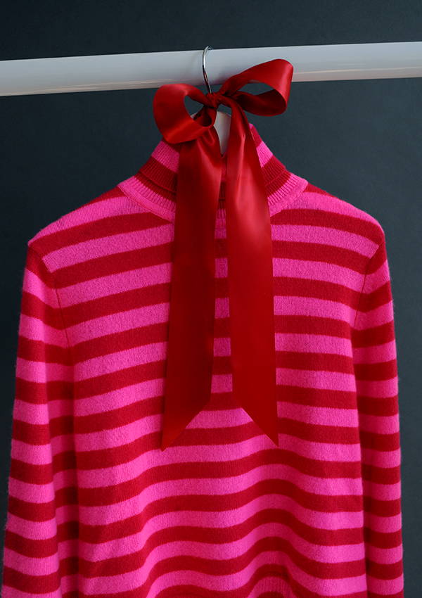 The Jumper 1234 Little Stripe Roll Collar in Cherry and Pink hanging on a rail with red ribbon.