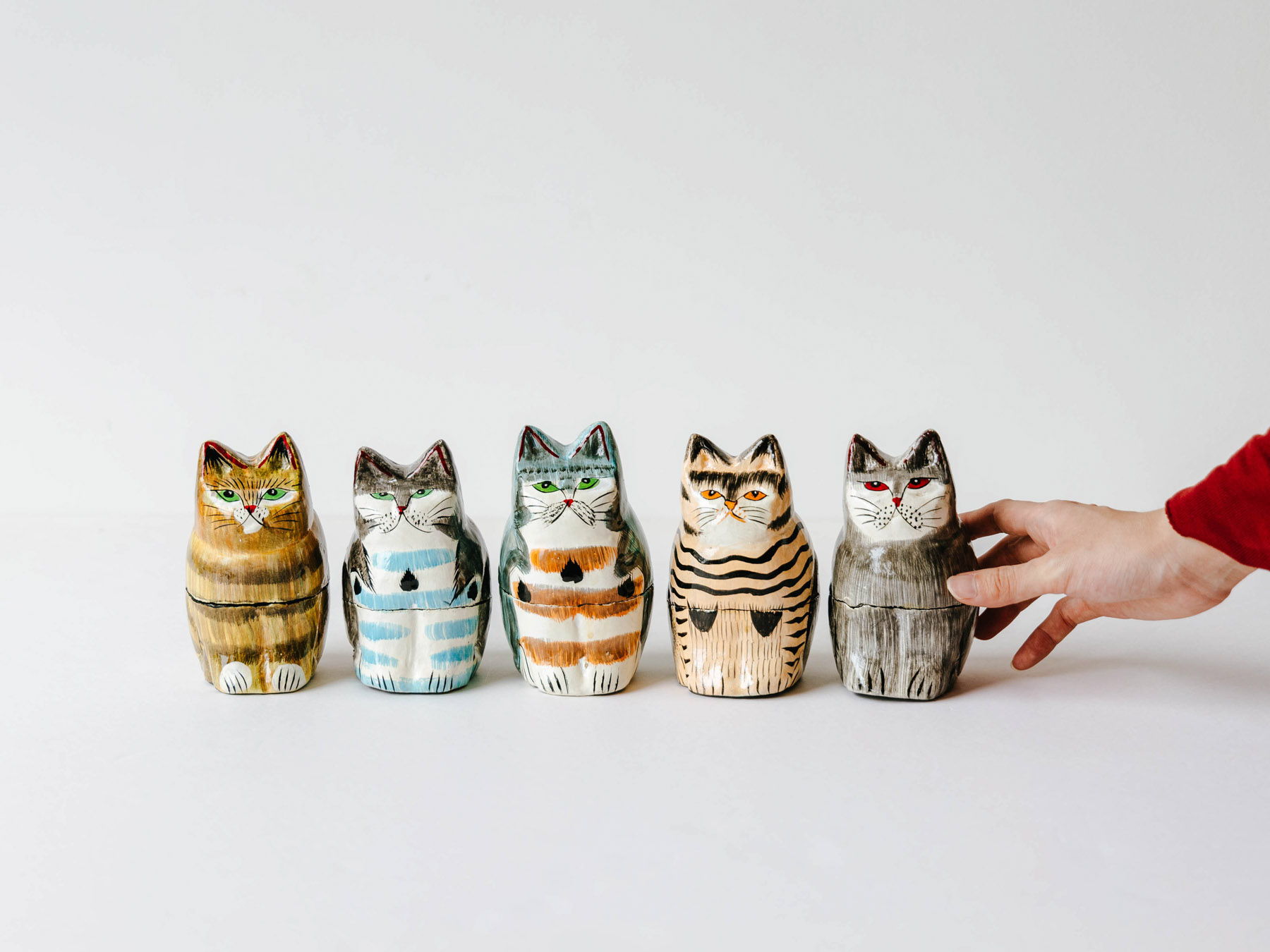 Colorful ceramic cat figurines lined up with a hand reaching for one.