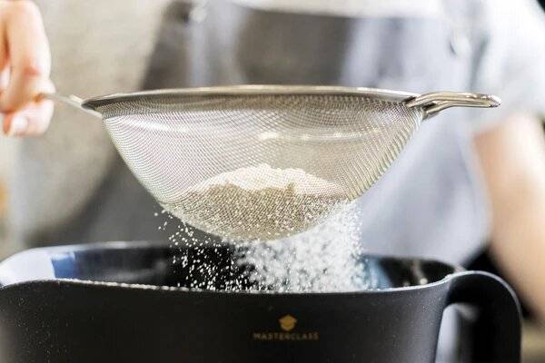 Flour being sieved into a bowl. 