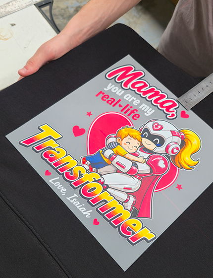 DTF printed film measured into place with a ruler, siting on a black hoodie featuring a retro comic-style 