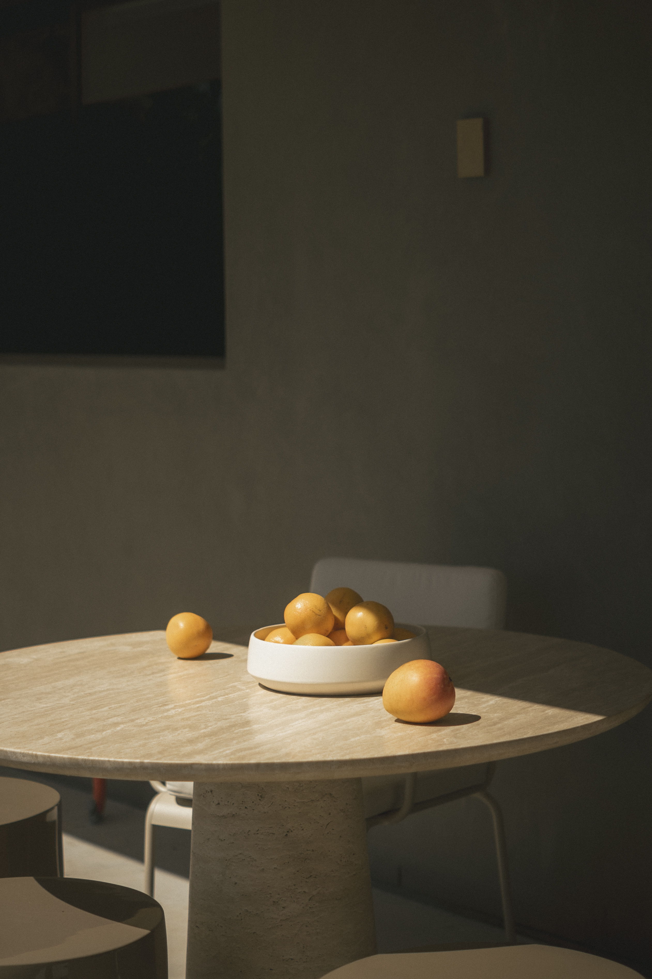 A round table with a bowl of oranges and a few scattered fruits.