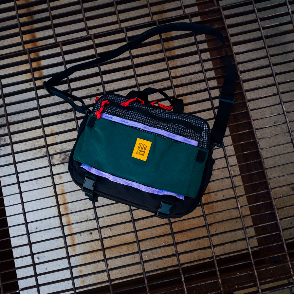 A green and black messenger bag on a metal grate.