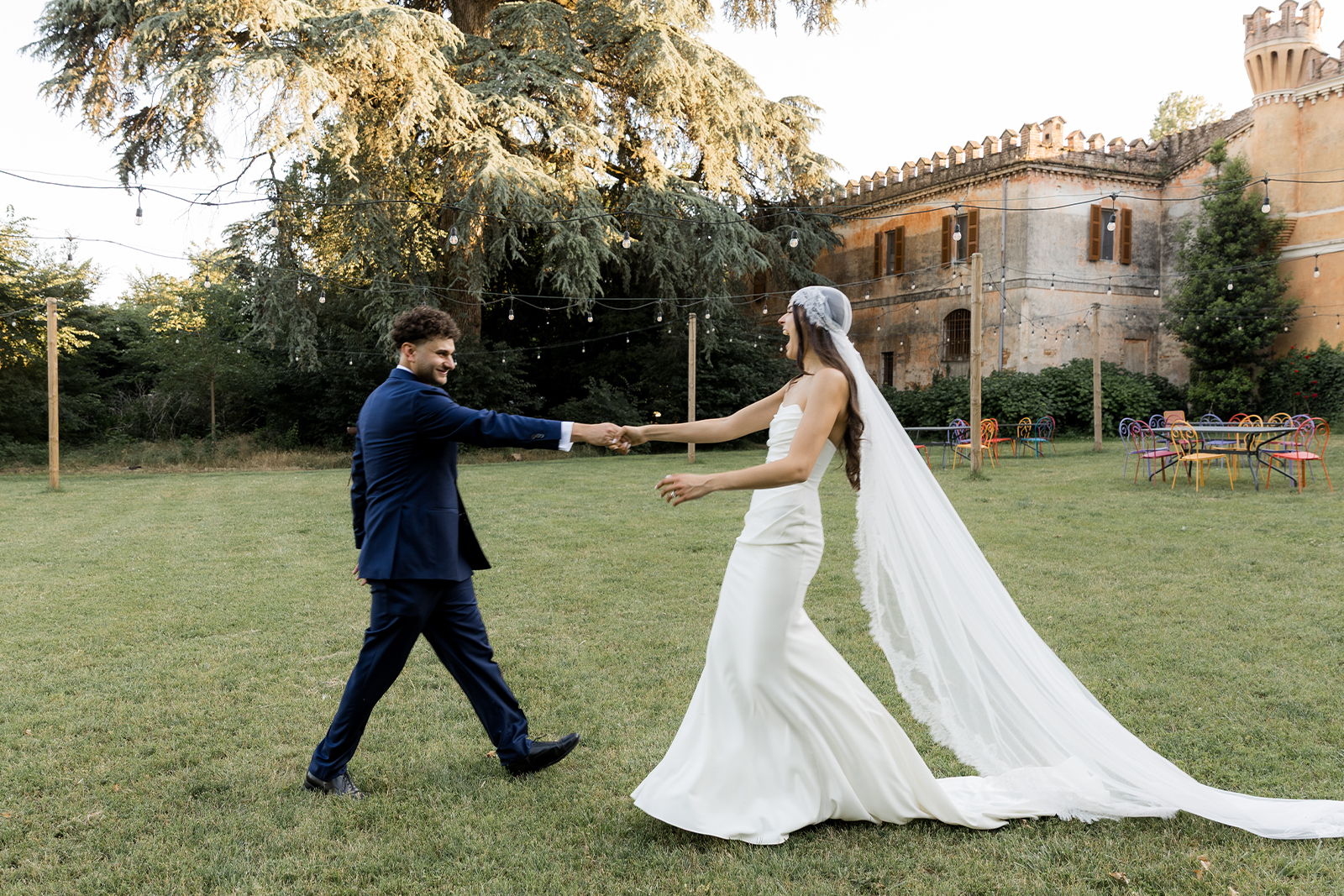 Bride and groom walking hand in hand on a grassy area.
