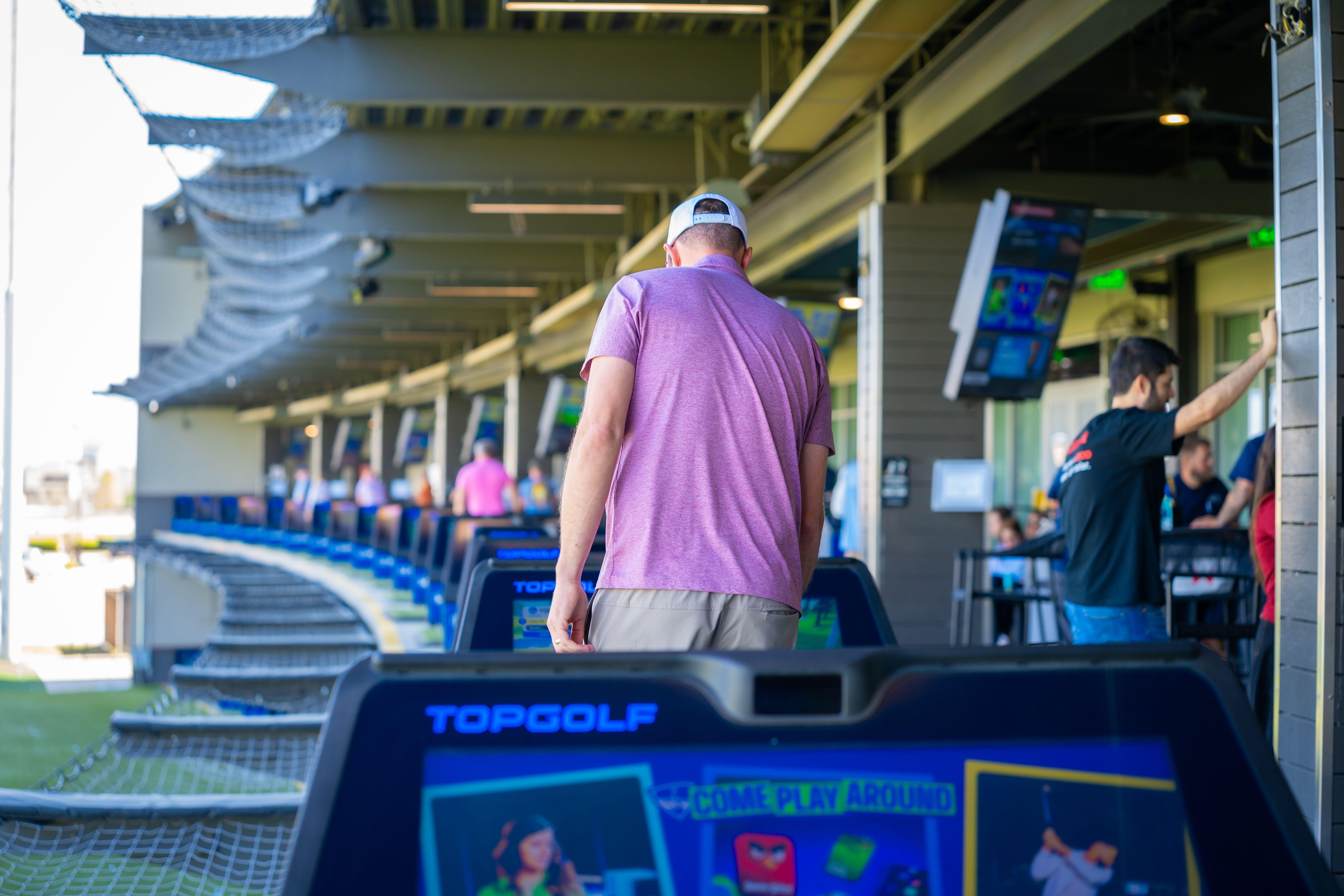 Person in a pink shirt at a Topgolf driving range.