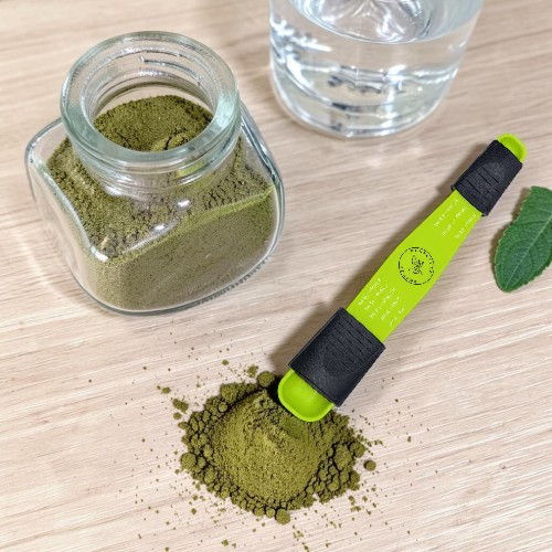 A jar of green powder with a measuring spoon on a wooden surface.